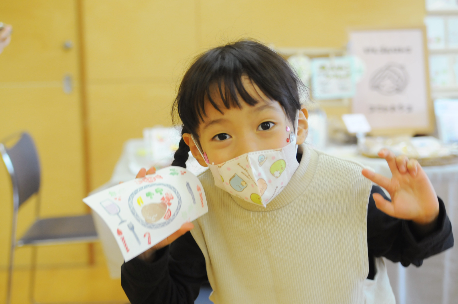 シャレール東豊中の新たな試み「マルシェ・ツクル・ゼミ」イベント「どんぐりまるしぇinぼん・しゃれーる」の消しゴムハンコブース「コニャハンコ」で完成したカードを手に笑顔の女の子