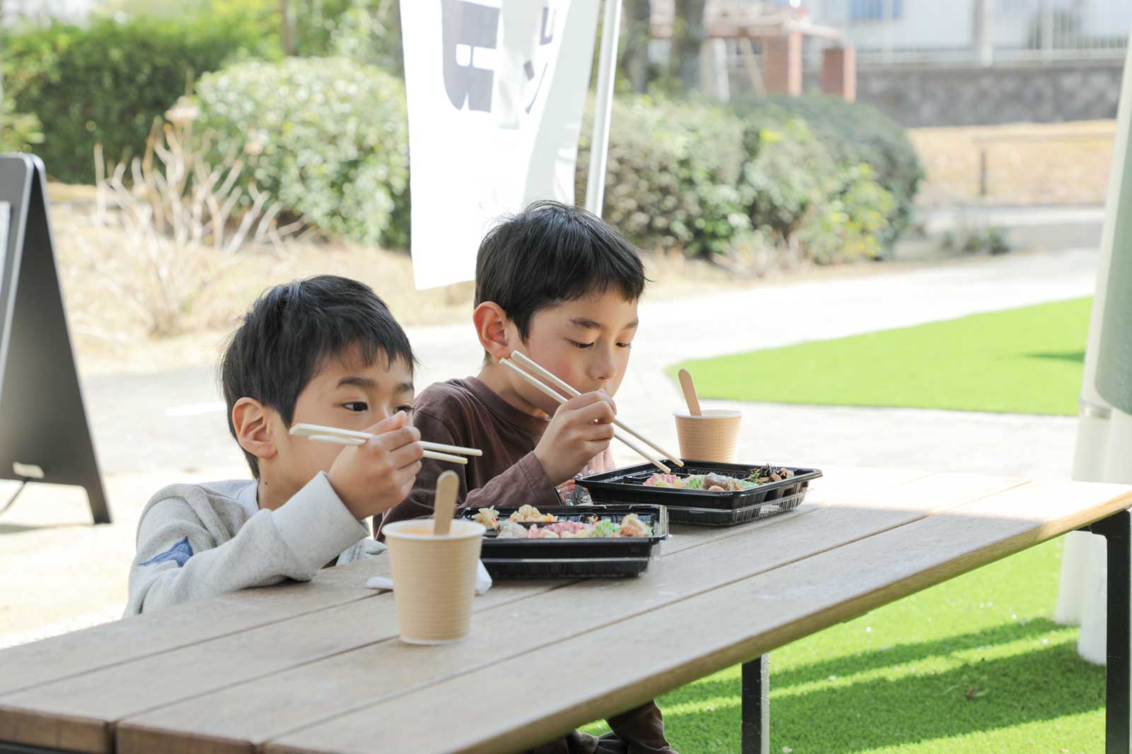 共用部にある人口芝でお弁当を食べる男の子たち