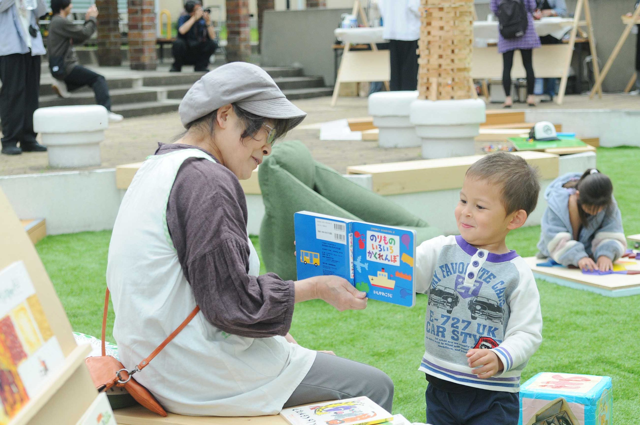 中宮第３団地でおこなわれたイベント「となりのひろば」で絵本の読み聞かせをする女性と絵本をゆびさす子ども