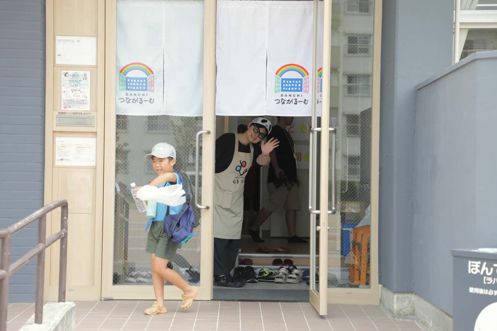 集会所から子どもを見送る藤井さん
